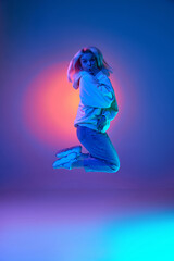 Surprise. Emotive young woman in casual clothes jumping over gradient multicolored studio background in blue neon light. Concept of emotions, facial expression, lifestyle, inspiration, sales, ad