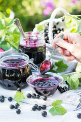 Cooked homemade black currant jam in small glass bowl and jars on white wooden table, fresh black currant jam close up, food and healthy eating concept