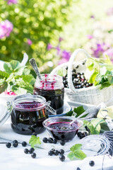 Cooked homemade black currant jam in jar on white wooden table background, fresh black currant jam...