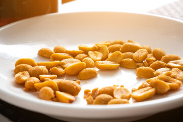 Pile of peanuts with salt and spices on white plate. Tasty snack.