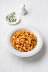 Simple pasta with tomato sauce sprinkled with fresh thyme in a white plate on a light gray background, top view, flat lay. Delicious homemade food