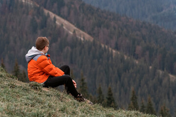 Naklejka na ściany i meble Travel hiking journey outdoor. Alone brown hair boy watch over valley and sits on the hillside