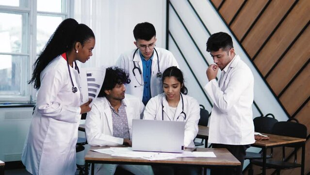 Young Medical Interns students in Medical Clothing Studying Together on laptop, the Results Chest X-Ray Scan of Patient. Multiethnic multiracial group of men and women learn to be a doctor 