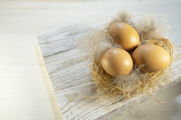 Three orange eggs lie in a nest on a table, on wooden boards. Easter card for the holiday. High quality photo