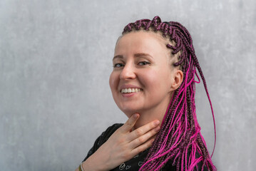 Portrait of cheerful young caucasian woman with pink artificial dreadlocks on gray background.