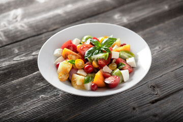 Salad with different varieties kind of red, yellow, green and black tomato mix, mozzarella cheese and basil. Caprese salas with fresh colourful tomatoes. Food photography