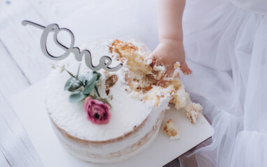 White cake. A cake with white cream and an inscription - one. First birthday. A child eats a cake with his hand. Delicious white cake on a white background. Children's birthday. Birthday decorations