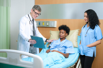 Obraz premium Young caucasian doctor with stethoscope holding clipboard physical health checkup report and nurse talking to african american patient lying in bed at hospital.Health care and medical concept.
