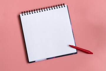 Mock up of empty scketchbook white paper on pastel pink background. One red wax crayon. Top view of open notebook with clean sheet. Copy space.
