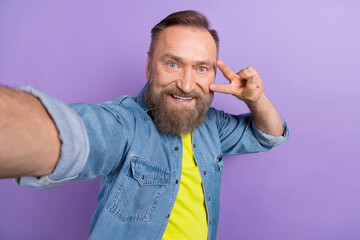 Portrait of cheerful granddad make selfie hand fingers show v-sign near eye isolated on purple color background