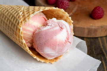 Waffle cone with white pink cream ice cream and raspberries