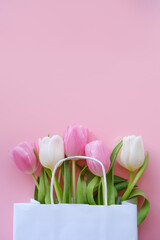 Pink tulips in a white paper bag on a pink background. Vertical image, flat lay, copy space.