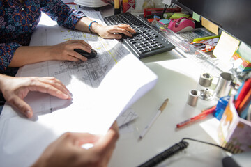 Hands of two colleagues at work in a technical office, working on the pc and examining a drawing