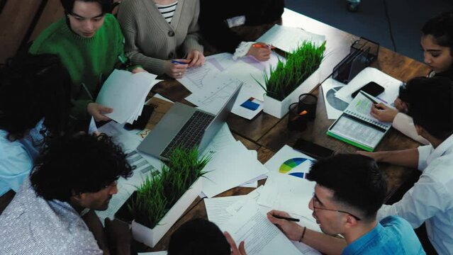 Young men and women brainstorming speaking about business in shared office sharing ideas. Communication and businesspeople concept. Multiracial students doing research assignment together at desk