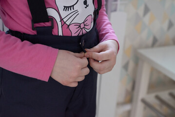 Close-up of hands that fasten a button on a jumpsuit. The child independently dresses for a walk