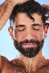 Fototapeta na wymiar Washing, hair and man in studio for skincare, grooming and hygiene against blue background. Haircare, body care and guy model relax in shower, happy and isolated on water splash, cosmetic or wellness