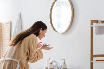 young brunette woman with closed eyes washing face in bathroom.