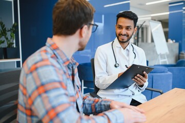 Indian doctor in white gown seeing patients in office.