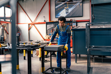 A worker moves metal plates using a table on wheels for easy transport in the workshop