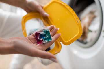 Cropped view of woman holding washing capsule and blurred box in laundry room.