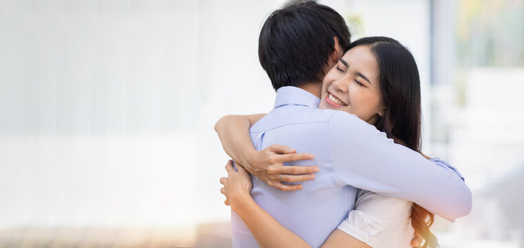 Attractive smiling Asian woman hugging man on urban indoor. Beautiful successful couple embracing in workplace. Husband and wife hug Togetherness concept