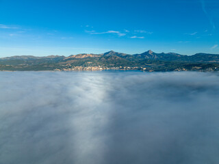 Fototapeta premium Aerial view, flight above the clouds, the coast of Mallorca in the fog with the town of Santa Ponca, Mallorca, Spain