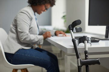 Disabled employee working in office. Orthopedic elbow crutches leaning on desk, with happy disabled...