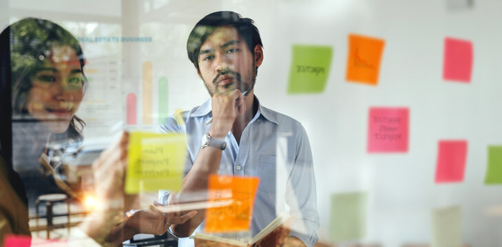 Young business people creative team using post it notes in glass wall to writing strategy business plan to development grow to success.