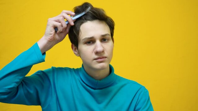 Boy in blue clothes comb his curly brown hair. Yellow horizontal background