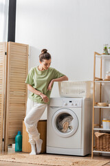 Young woman looking at laundry in washing machine in laundry room.