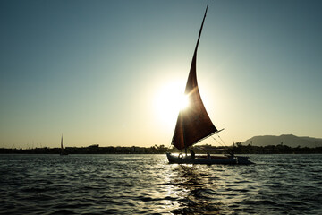 sailing boat on the nile at sunset. Sunbeams illuminate sails. nile in luxor egypt - obrazy, fototapety, plakaty