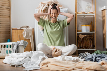 stressed young woman sitting near clothes on floor in laundry room.