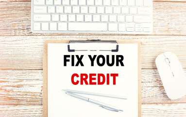 FIX YOUR CREDIT text on a clipboard with keyboard on wooden background