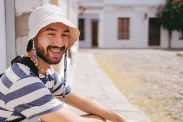 Young latin man looking at camera with a smile while wearing a bucket hat in a colonial...