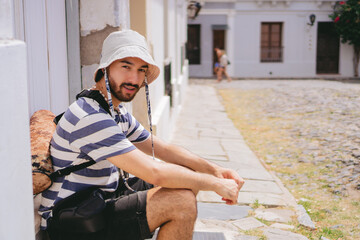 Young latin man with a tripod on his back and wearing a bucket hat in Colonia del Sacramento. Copy...