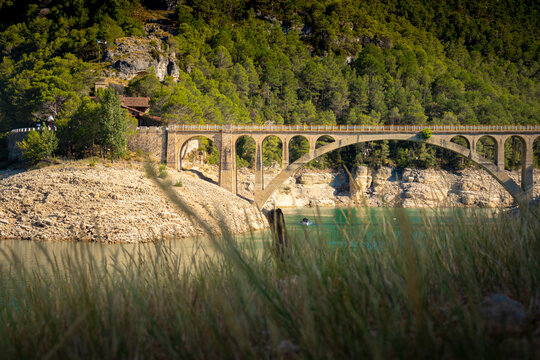 Historic stone bridge over turquoise river with forested mountains. Ulldecona reservoir, valencia, spain - Powered by Adobe