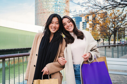 Portrait of two multiracial women carryng shopping bags and smiling looking at camera. A couple of happy females standing outdoors at the mall. Lifestyle concept. High quality photo