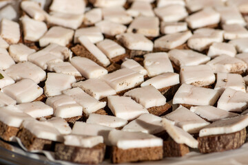 Pieces of lard or bacon, sliced thinly for consumption with black rye bread on a wooden cutting board in a street food market, close up