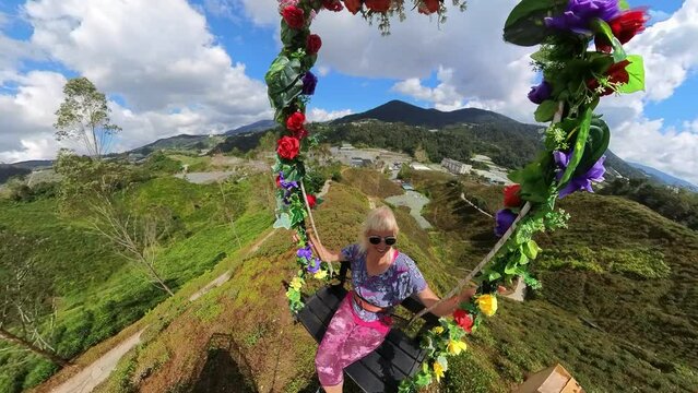 A traveler woman soared on a swing, taking in the stunning aerial views of tea farms in the Cameron Highlands of Malaysia. The tea leaves produced here are top-notch quality.