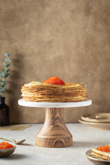 Stack of thin pancakes or crepes decorated red caviar on a marble stand with wooden leg. Maslenitsa concept. Shrovetide traditional russian food. Copy space. Brown background