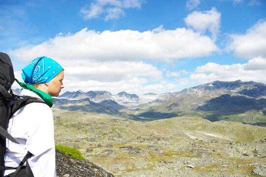 Red-haired girl with a backpack in the mountains of the Jotunheimen National Park in summer day