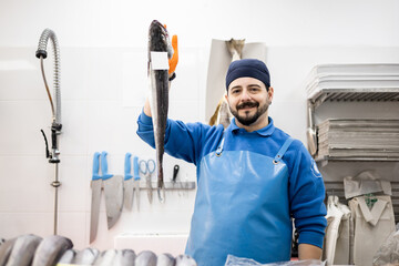 A middle-aged fishmonger in apron and hat is teaching the camera a fish, food sales, concept of small and medium enterprises.