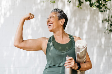 Elderly woman celebrates her fitness achievements by flaunting her bicep outdoors - obrazy, fototapety, plakaty