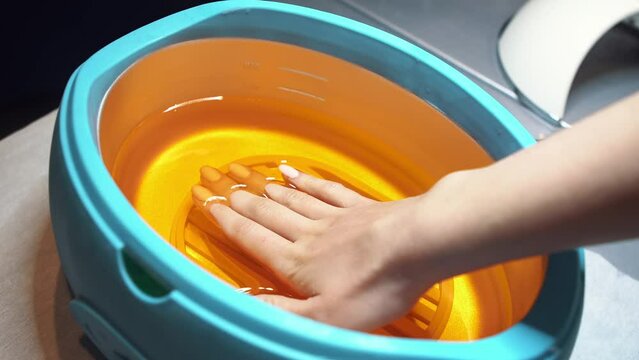 Paraffin bath. Spa Salon. Manicure. Process paraffin treatment. Female hand and orange paraffin wax in bowl. Manicure and skincare. Woman girl in beauty spa salon. Process of paraffin therapy of hand