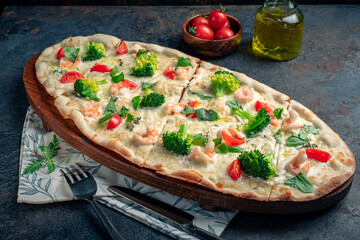 Long pizza with broccoli, tomatoes, basil and shrimp. Extra-sized Italian pizza, served on a wooden board, close up