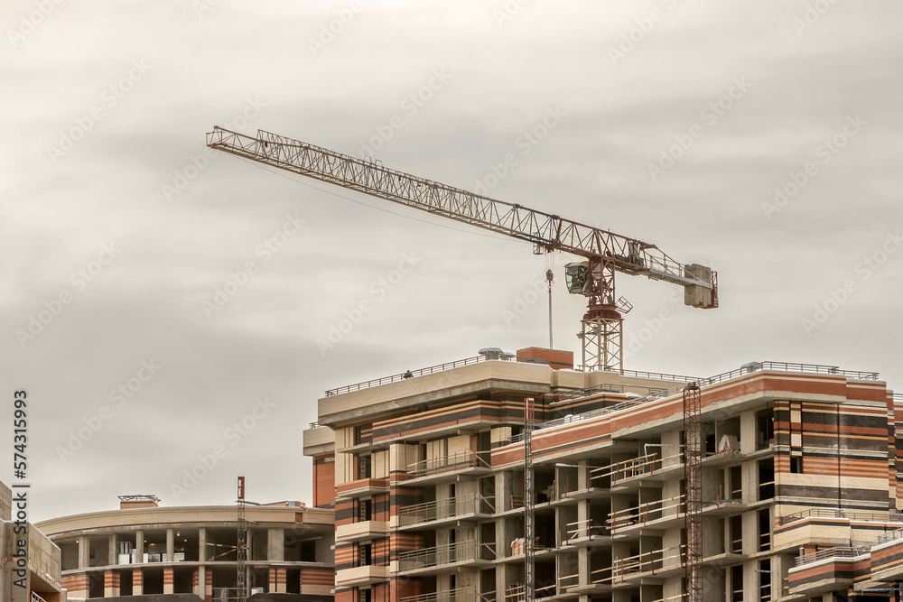 Wall mural a construction crane against the background of a sky with gray clouds and a multi-apartment building