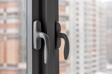 Handles for opening a gray metal-plastic window, against the background of an apartment building under construction