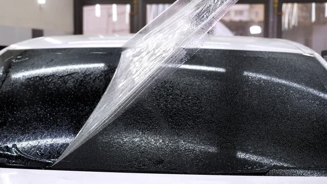 A close-up of a car service master splashing water on the glass before gluing tinted film in an auto repair shop. The process of tinting the car.