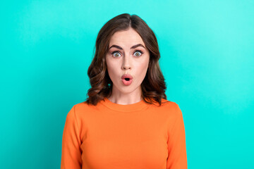 Fototapeta premium Portrait of young funny shocked woman brown curly hair wear stylish orange top pouted lips shocked news isolated on aquamarine color background