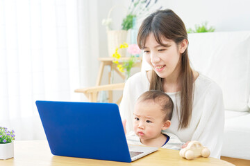 家で赤ちゃんとパソコンを見る母親